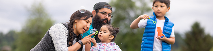 A family is playing outside with the two kids blowing bubbles